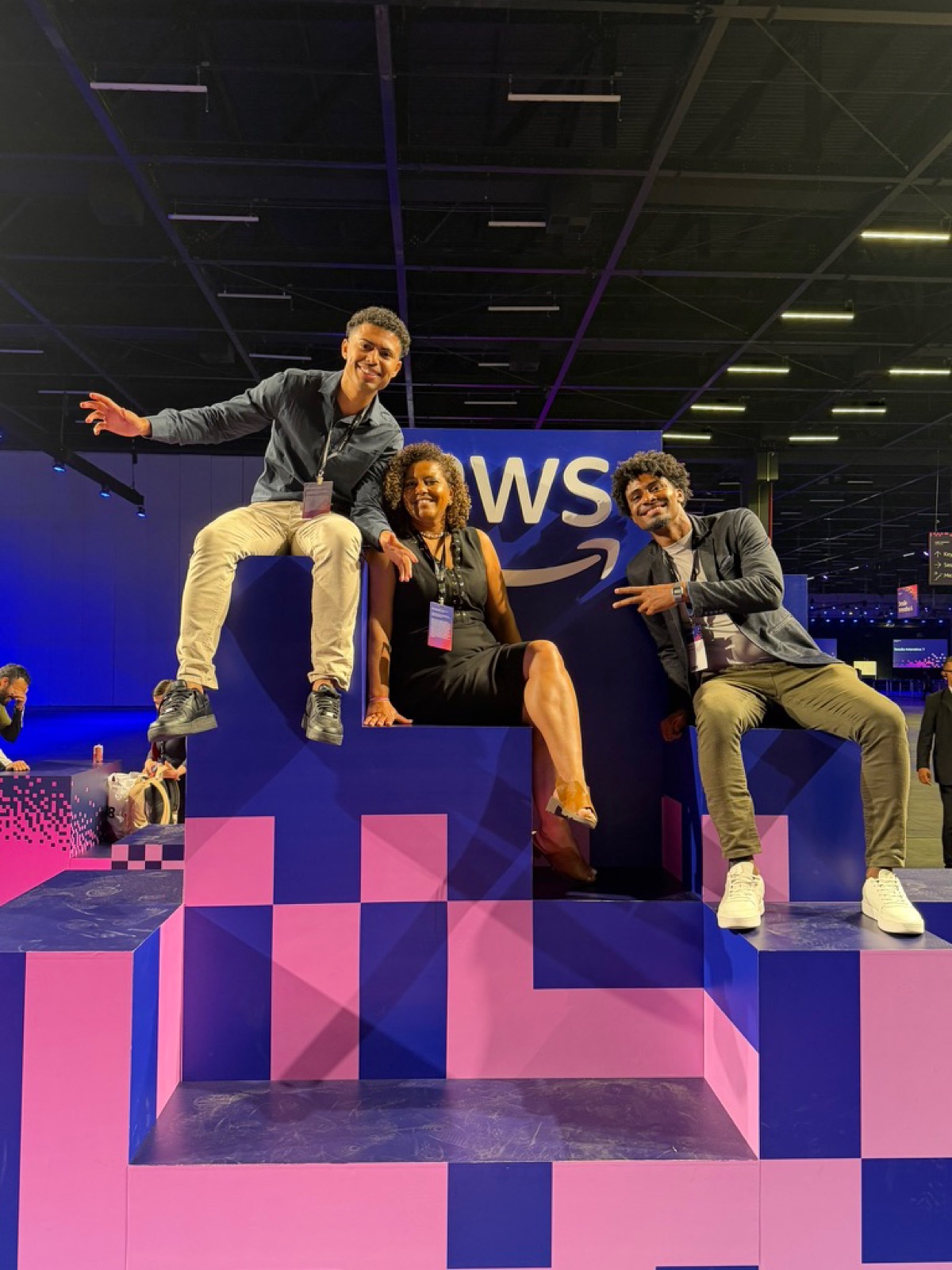 Três pessoas sentadas no letreiro pixelado da AWS no AWS Summit São Paulo